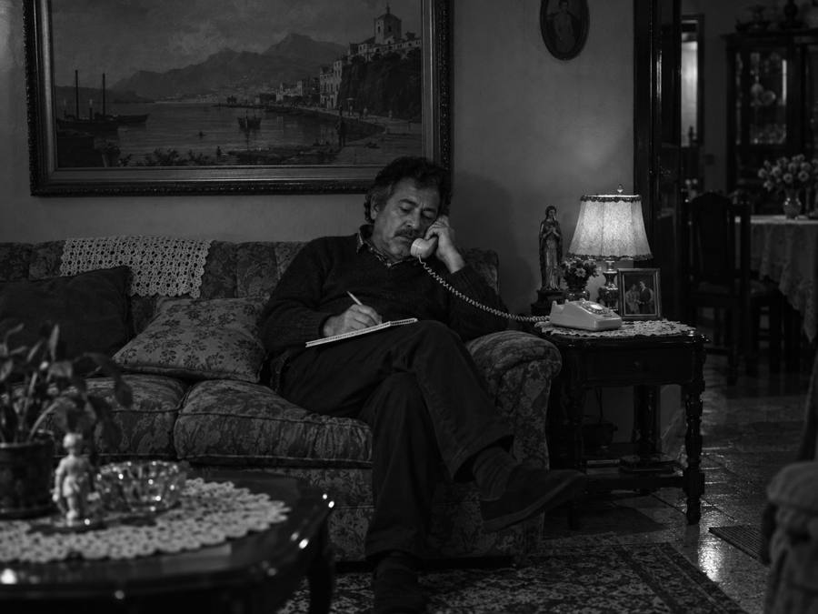 Hombre en el sofá de su sala, hablando por teléfono y tomando notas.