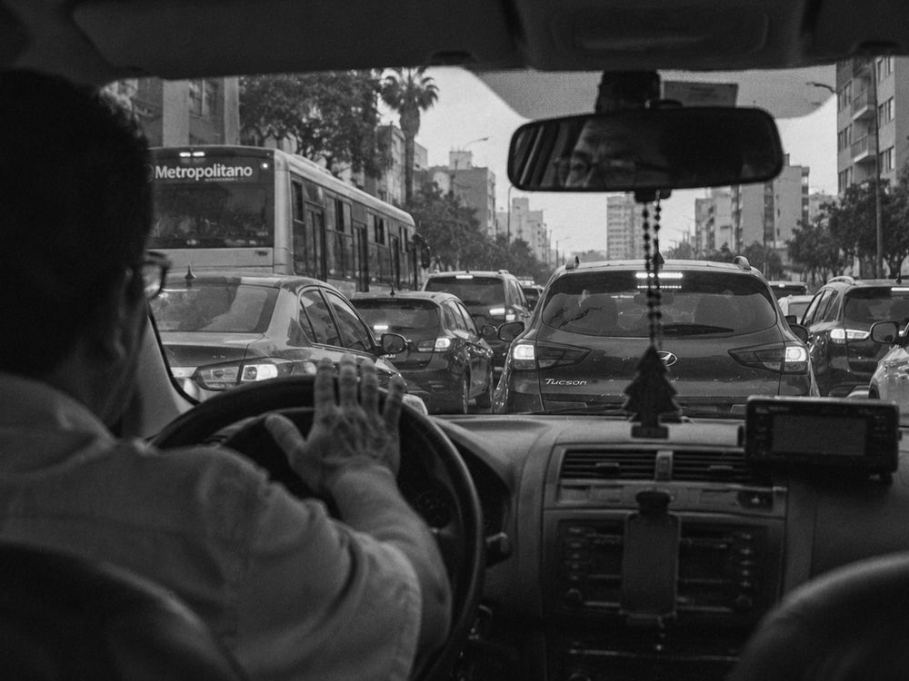 Fila de autos detenidos ante un semáforo en rojo; un conductor con la palma sobre el claxon.