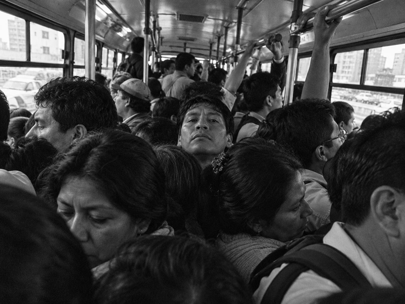 Interior de un bus repleto; un pasajero en el centro mira a cámara, sin agarrarse de nada.