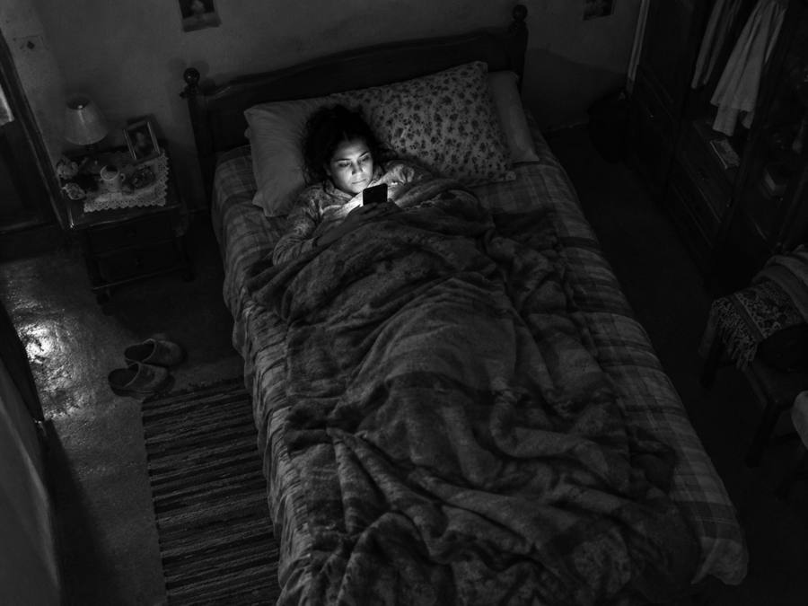 Mujer en la cama a oscuras, con la cara iluminada por la pantalla del celular.